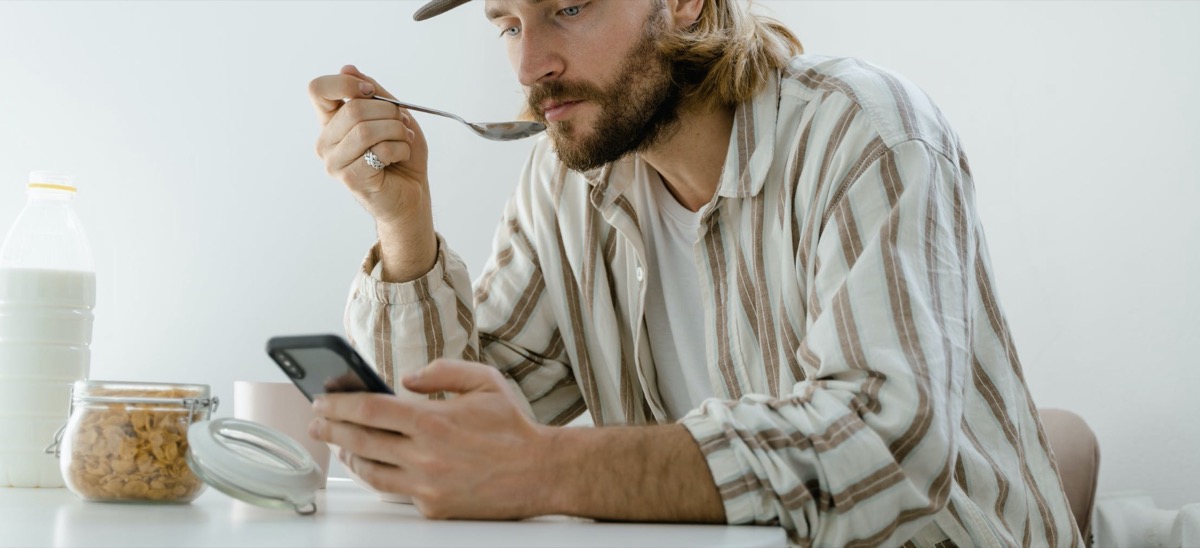 Man eating breakfast while scrolling phone 
