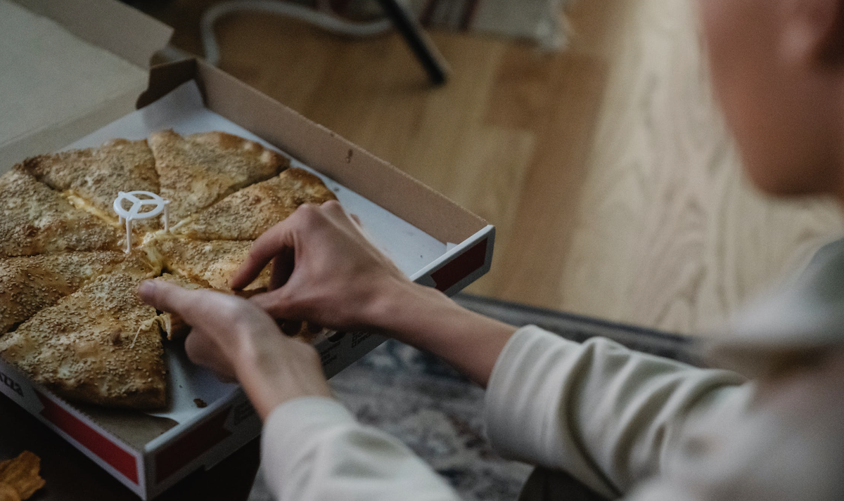 Woman taking out a slice of pizza from box. Image: Pexels - Eren Li